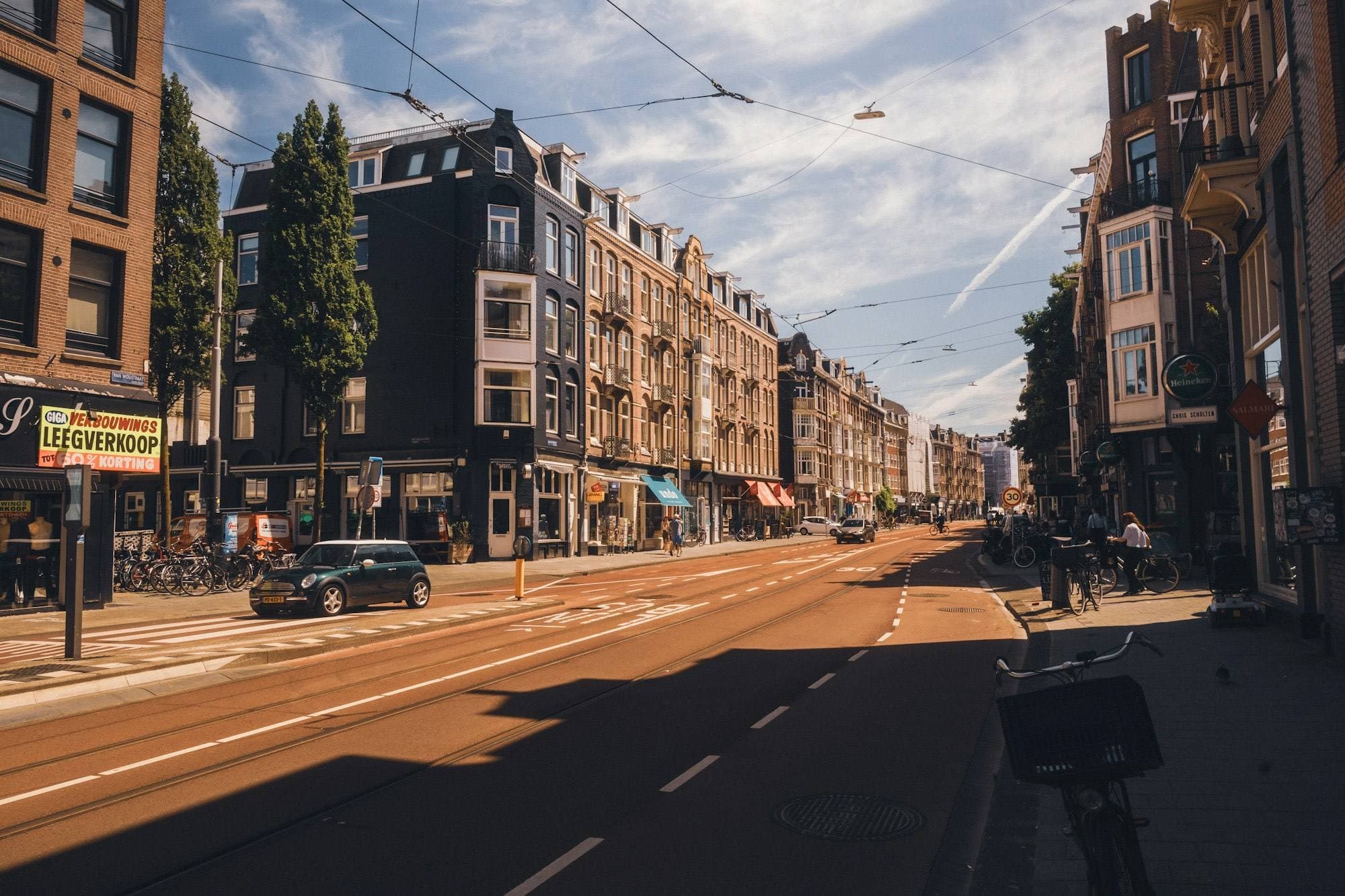 Zonnige Amsterdamse straat met tramrails, fietspad en geparkeerde auto’s