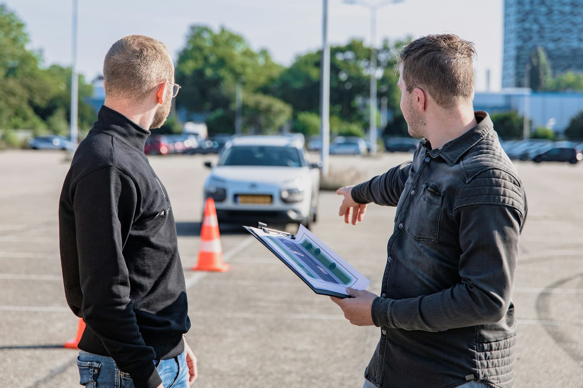 Instructeur met klembord legt een leerling een manoeuvre uit op een oefenterrein met pionnen