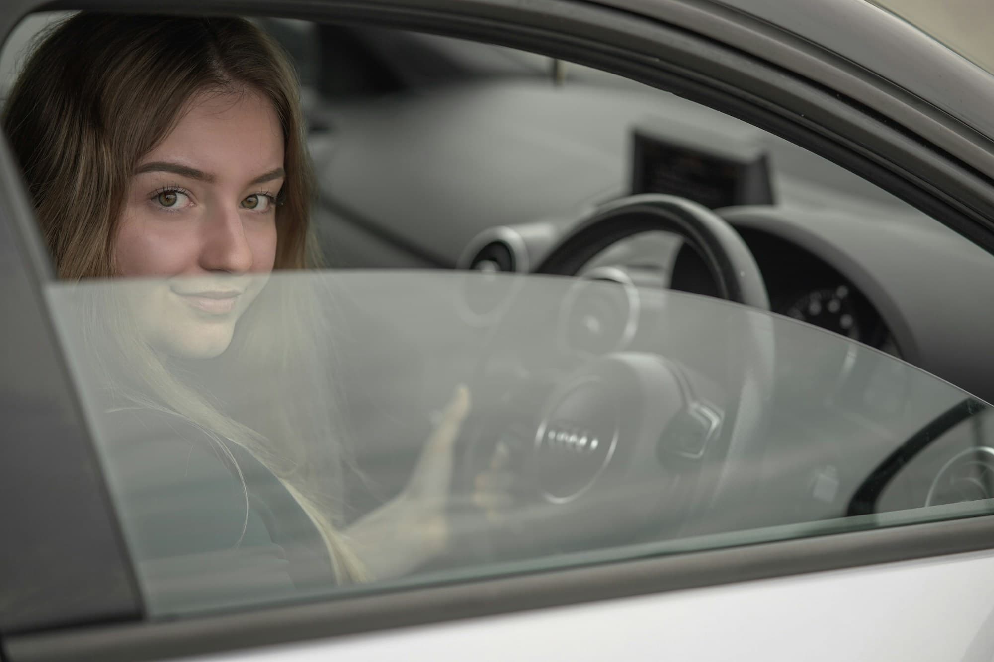 Jonge leerling achter het stuur kijkt glimlachend door het zijraam